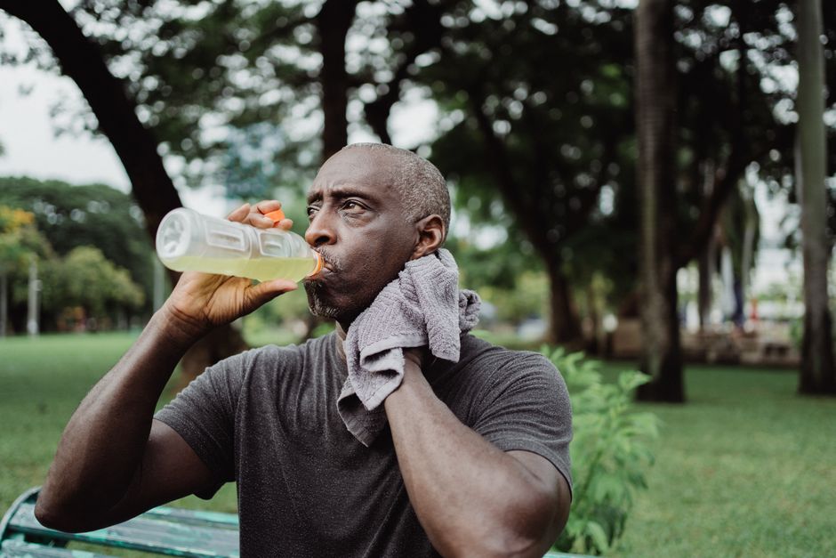 Adult man drinking sports beverage and wiping sweat in a park.