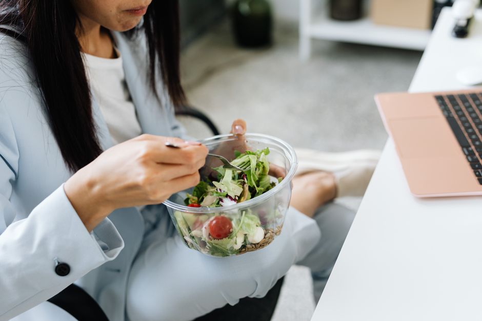 Adult woman eating a vegetable salad at her office desk, embodying healthy lunchtime habits.
