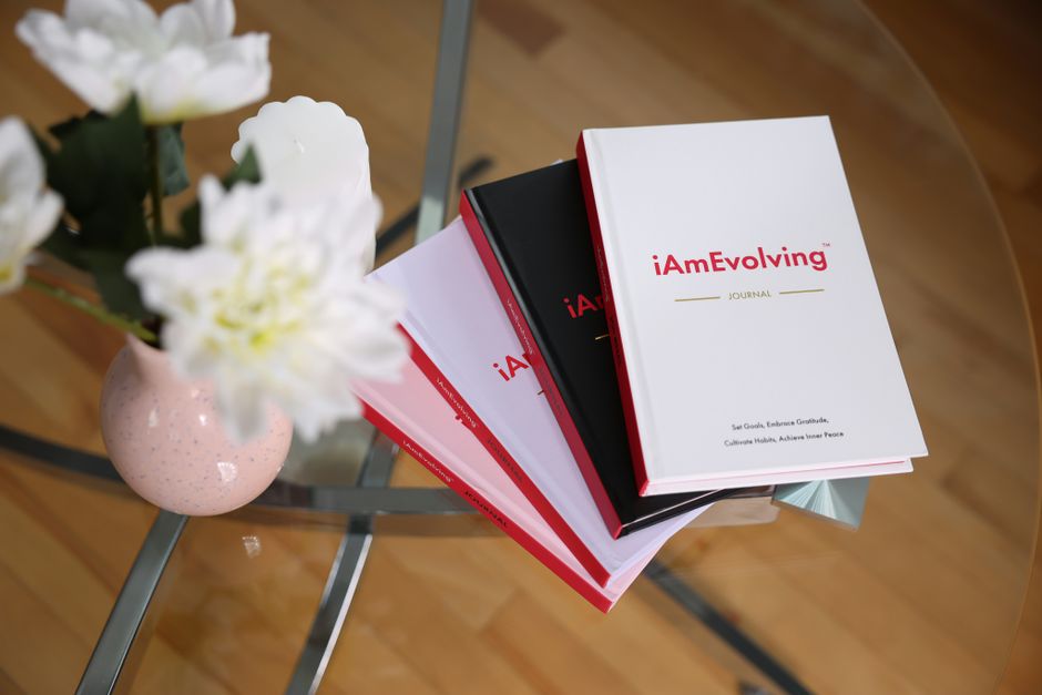 An elegant journaling scene featuring iAmEvolving books and white flowers on a glass table, ideal for self-care.