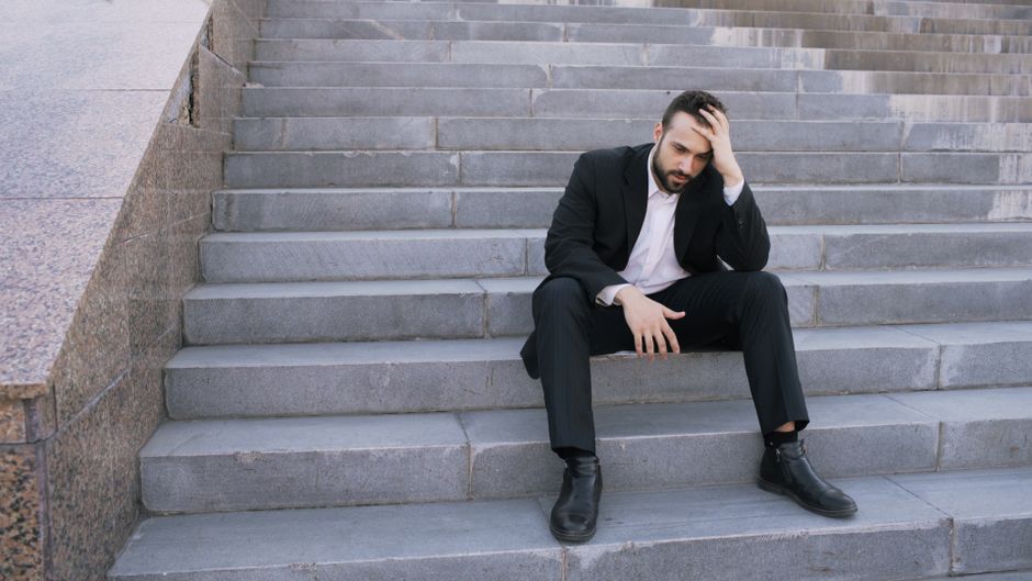 Businessman in a suit sitting distressed on concrete stairs, facing challenges.