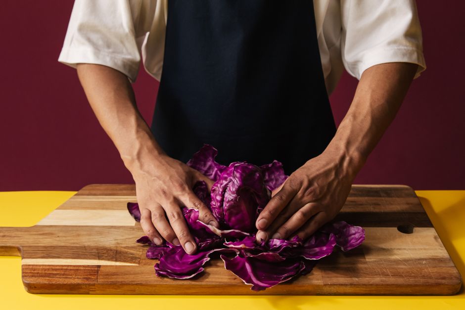 Chef in apron handling red cabbage on wooden board, showcasing food preparation in a kitchen setting.