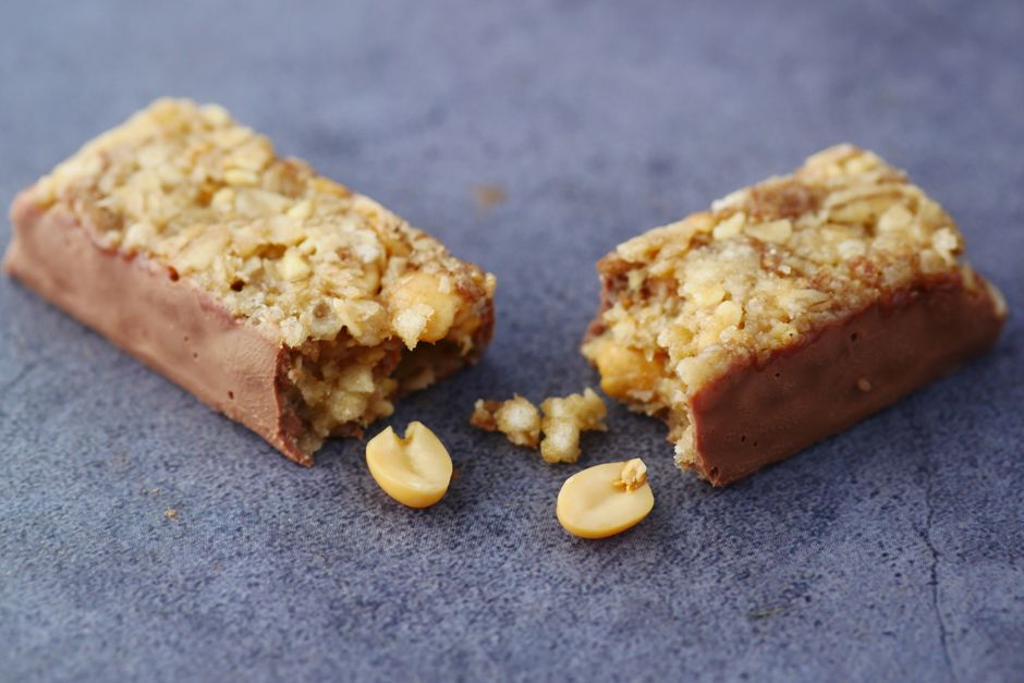 Close-up of a broken chocolate and nut energy bar on a gray surface.