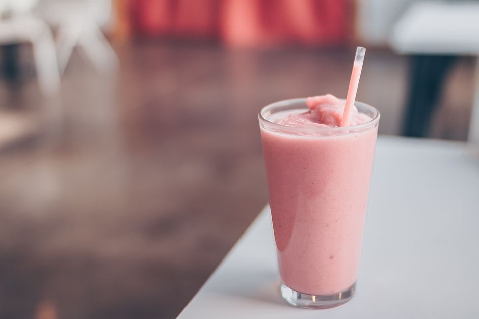 Close-up of a delicious strawberry smoothie served in a glass with a straw on a table.