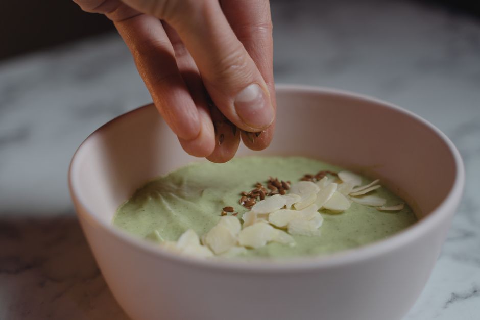 Close-up of a hand adding toppings to a nutritious green smoothie bowl with almonds and seeds.