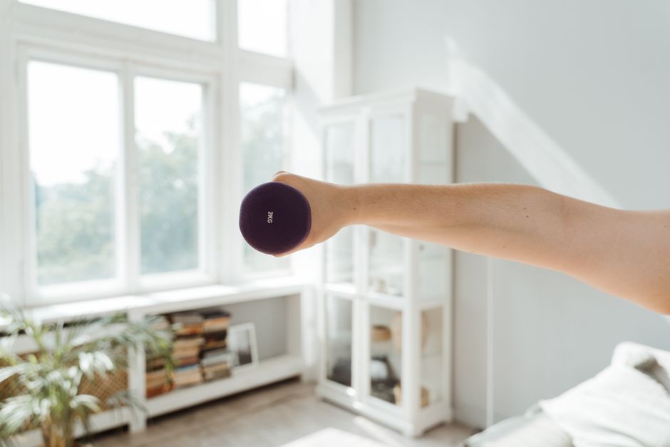 Close-up of a person lifting a 2kg dumbbell in a sunlit room.