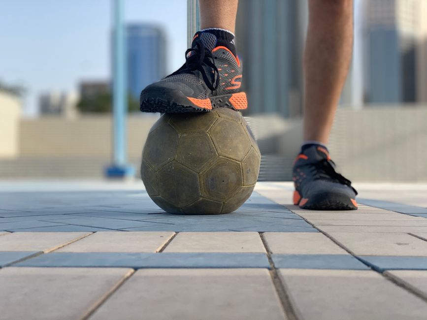 Close-up of a sneaker-clad foot balancing on a soccer ball in an urban setting.