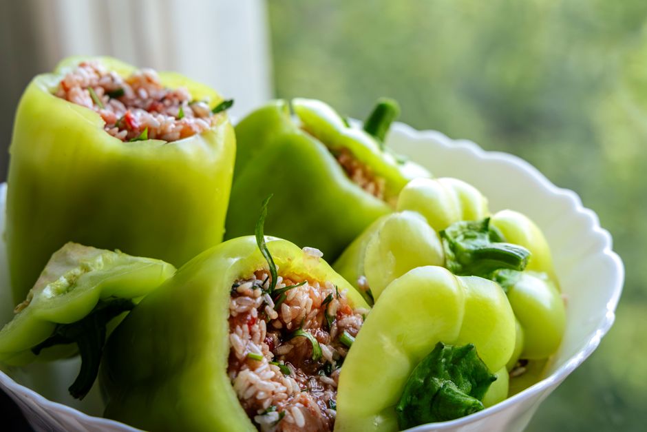 Close-up of fresh green bell peppers stuffed with rice and herbs, served in a white bowl against a blurred background.