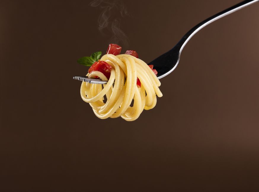 Close-up of spaghetti with tomato and basil garnish on a fork against a brown background.