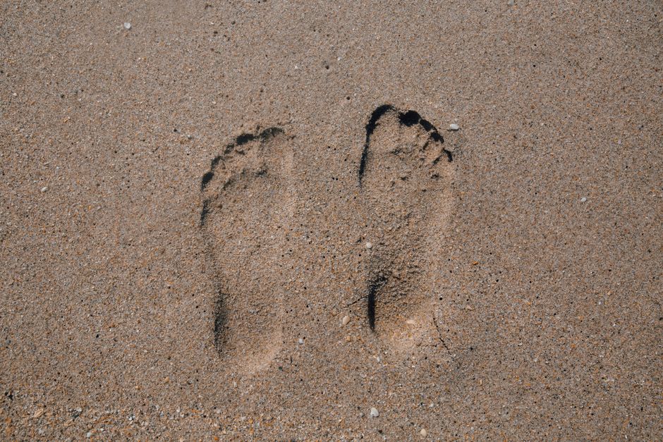 Close-up of two footprints in sand, evoking summer beach vibes.