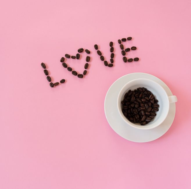 Coffee bean arrangement spelling 'LOVE' beside a cup on a pink background. Perfect for coffee lovers.