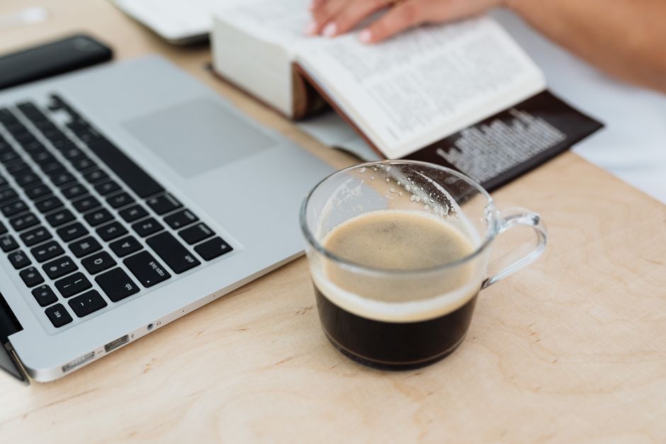 Cozy workspace setup with a laptop, book, and coffee cup on a wooden desk.