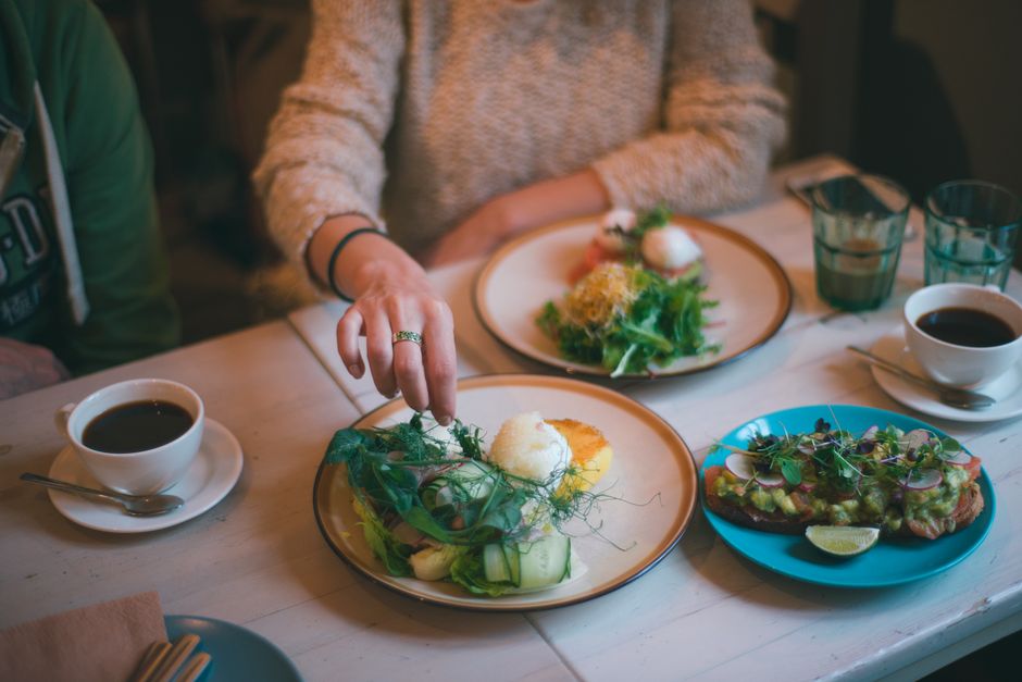 Crop anonymous female eating healthy meal served on plate with coffee on table in restaurant
