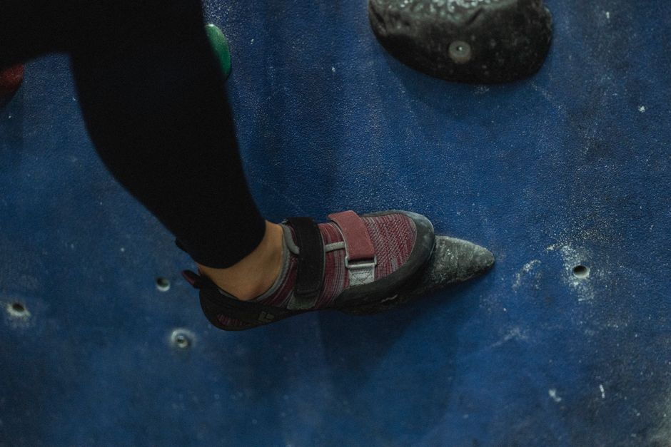 Crop unrecognizable female mountaineer putting leg on grip while ascending climbing wall in gym