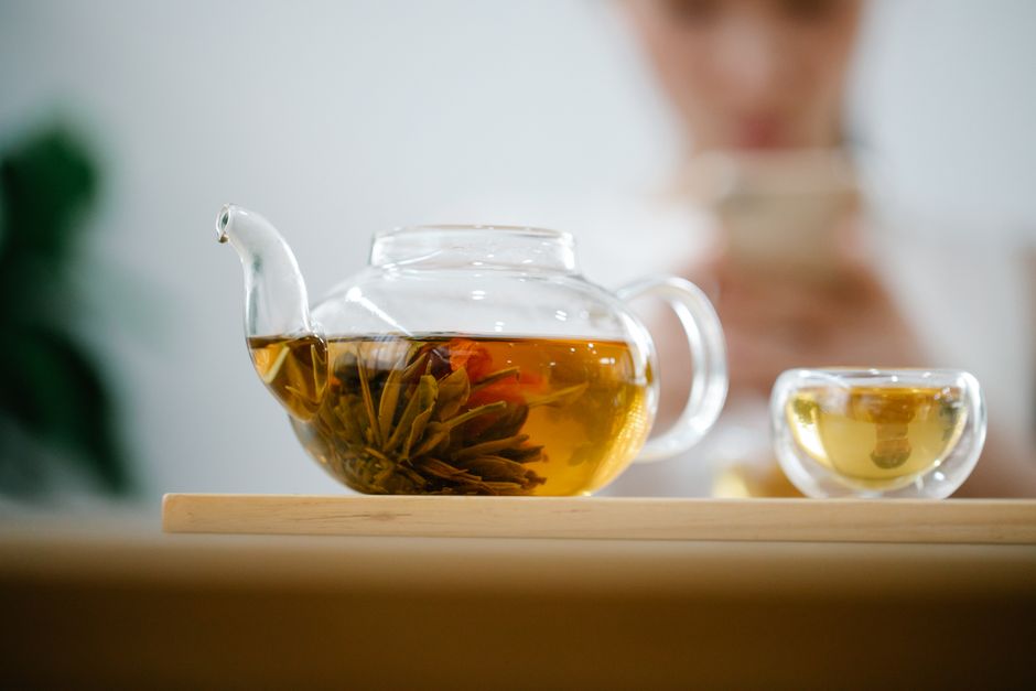 Elegant glass teapot with brewed herbal tea on a wooden tray, perfect for relaxing moments.