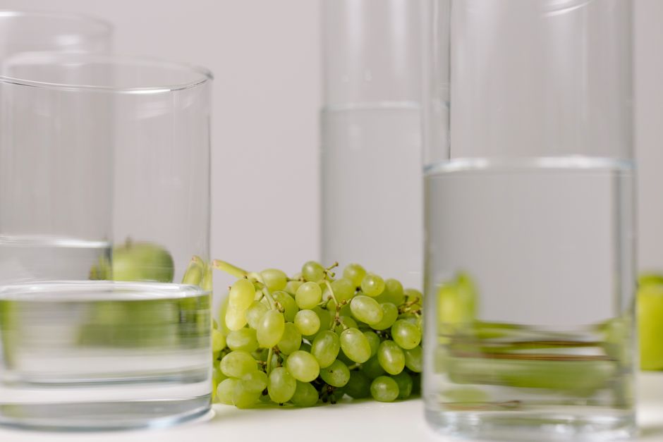 Elegant minimalist still life of green grapes and transparent water glasses on a white surface.