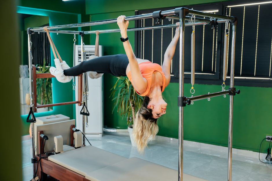 Fit woman doing Pilates on reformer equipment in a gym, showcasing strength and flexibility.