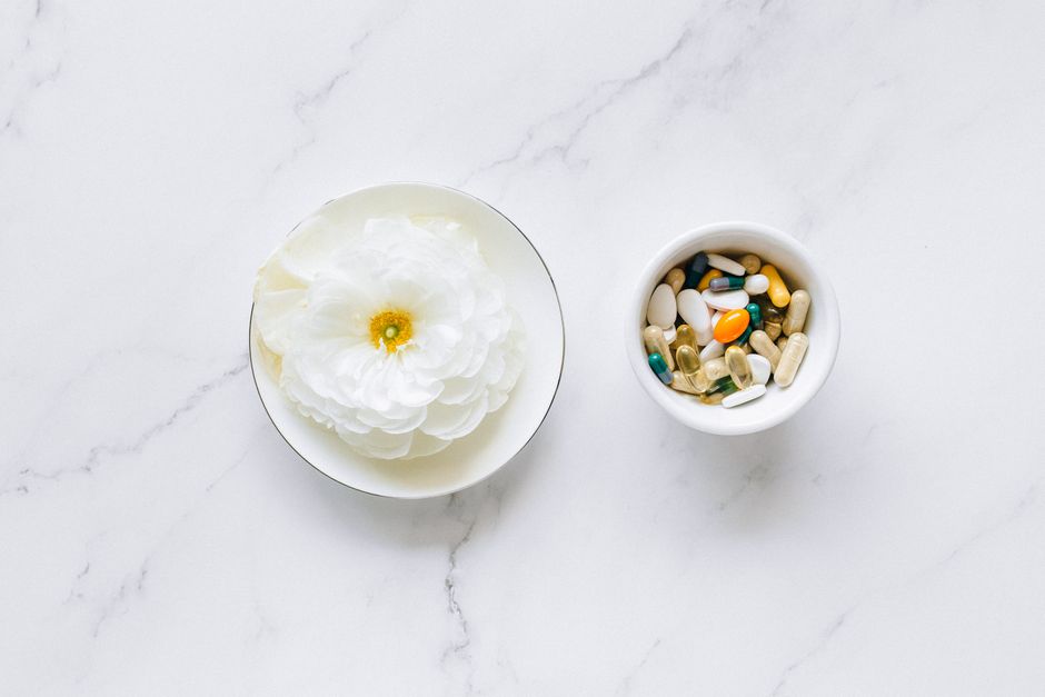 Flat lay of a white flower next to mixing pills on a marble surface, symbolizing natural vs synthetic remedies.