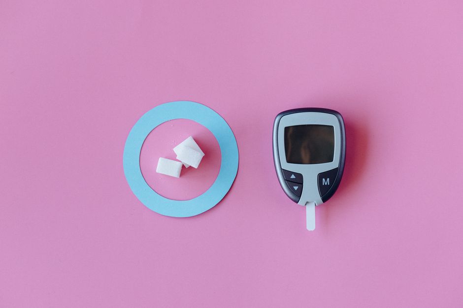 Flat lay of glucometer with sugar cubes on pink background, symbolizing diabetes awareness.