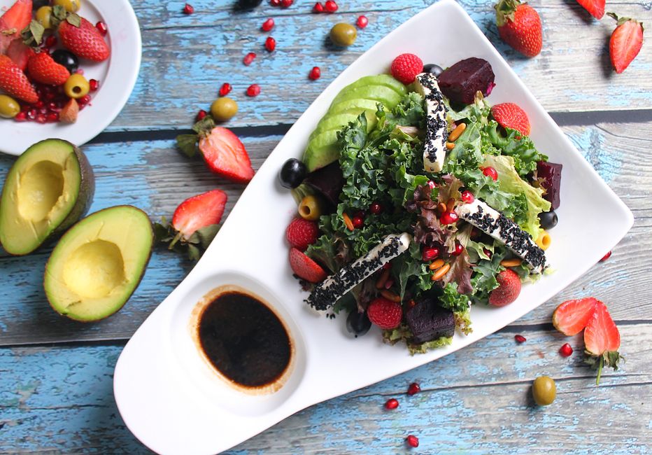 Fresh and nutritious salad featuring avocado, strawberries, and diverse greens, served on a white plate with rustic blue wooden background.