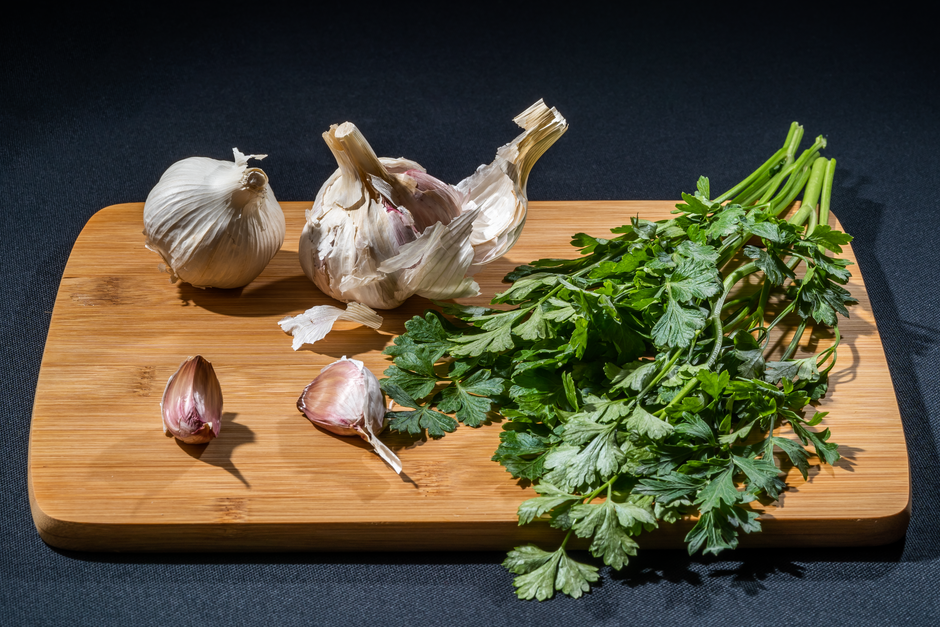 Fresh garlic bulbs and parsley leaves arranged on a wooden cutting board, perfect for culinary and cooking stock images.