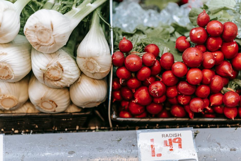 Heap of fresh red radish near pile of fennel placed on shelf with price in light grocery store with vegetables