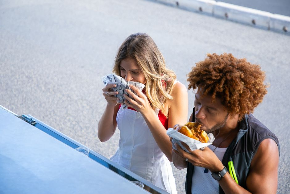 High angle of diverse hungry couple having lunch with burgers together at food truck