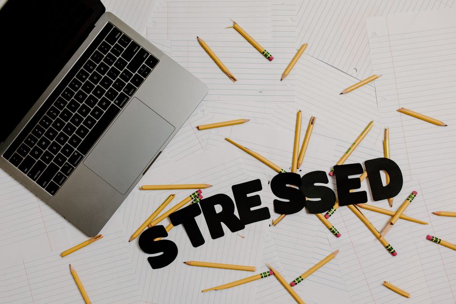 Image of a cluttered desk with laptop and scattered pencils spelling 'stressed,' symbolizing burnout and overwork.
