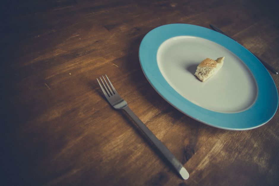 Minimalist bread piece on a blue-rimmed plate with fork and knife on wooden table.