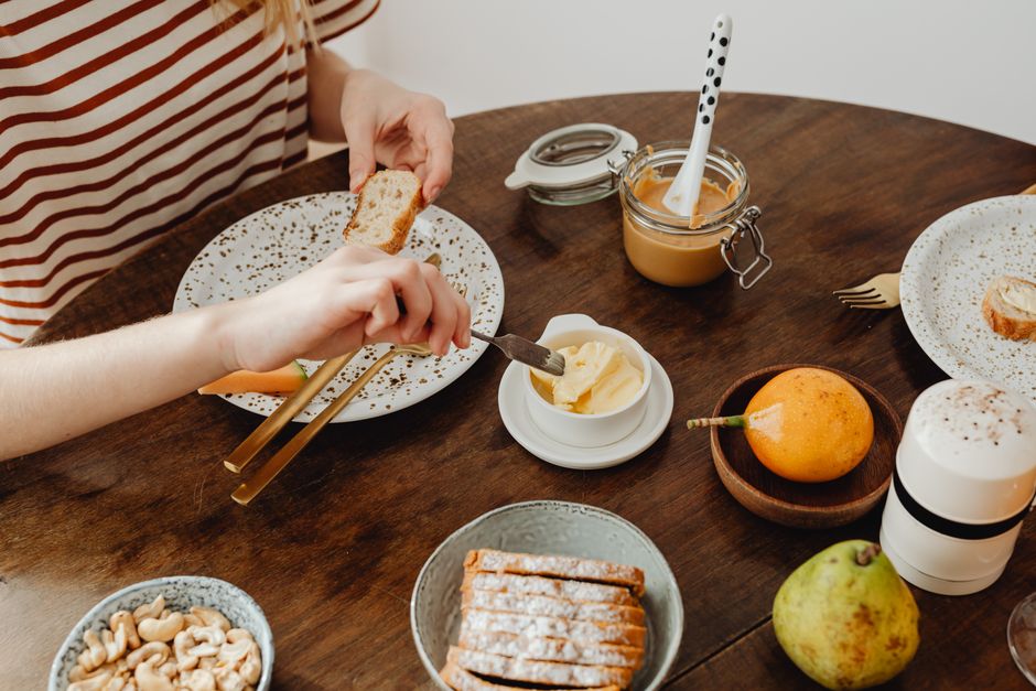 Overhead shot of a rustic breakfast scene with bread, butter, fruits, and nuts on a wooden table.