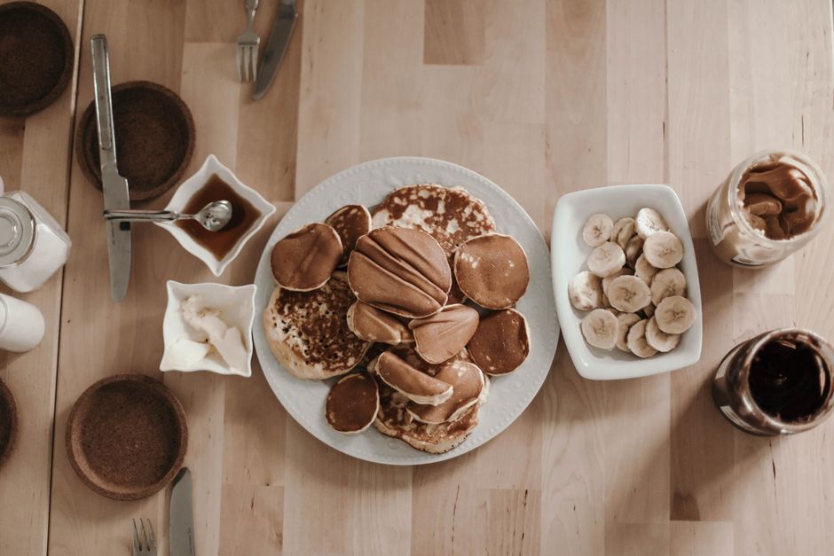 Overhead view of a breakfast table with pancakes, banana slices, and spreads.
