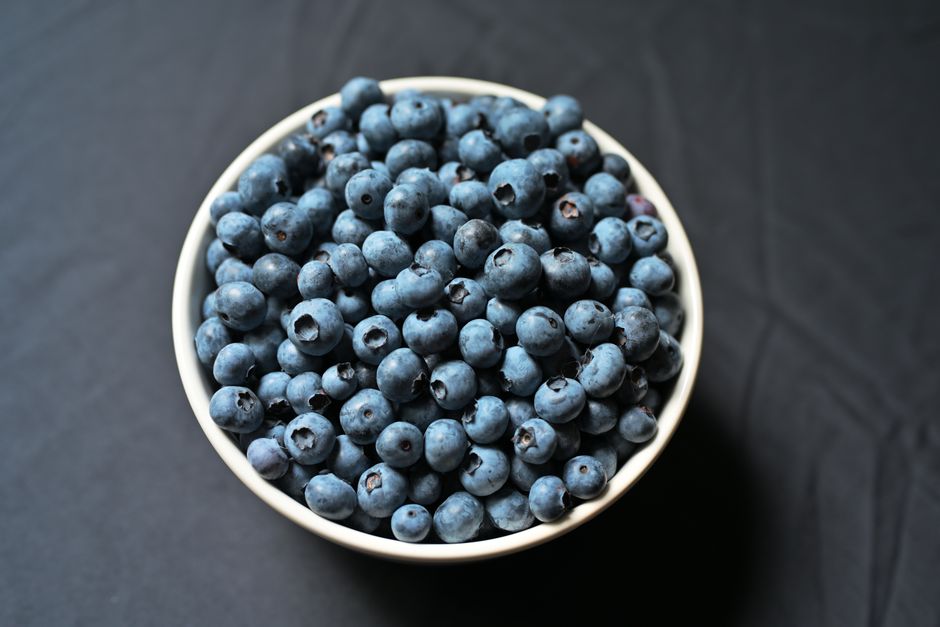 Overhead view of a vibrant bowl of blueberries on a sleek black backdrop, highlighting their freshness.
