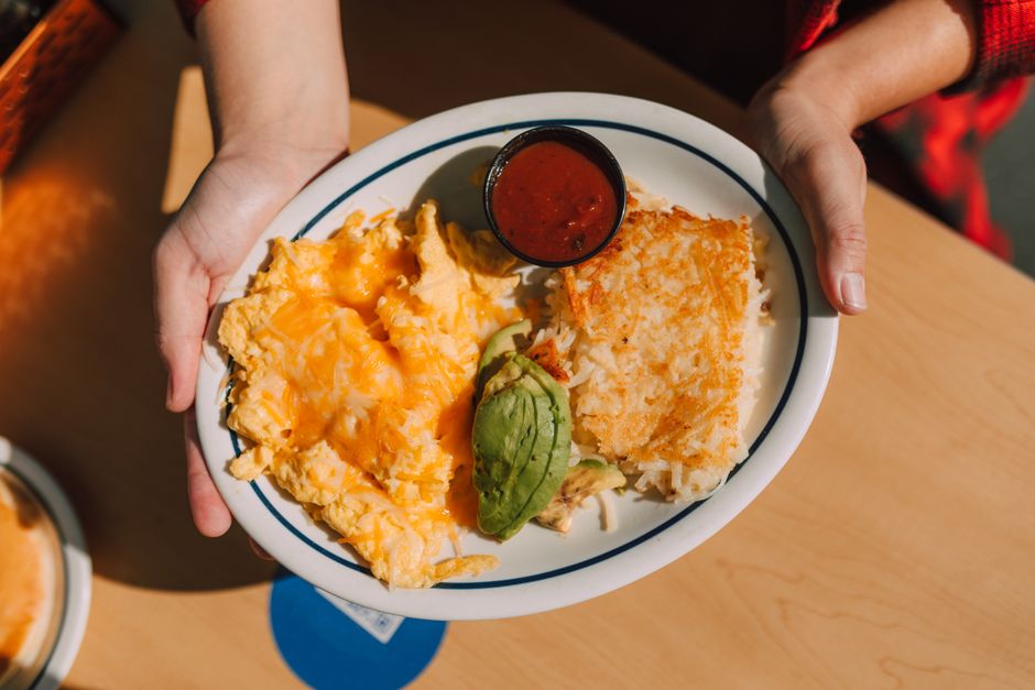 Plate of cheesy scrambled eggs, avocado, hash browns, and sauce, perfect for breakfast.