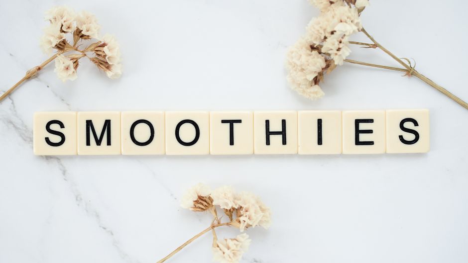 Scrabble tiles spelling 'Smoothies' on marble surface with floral accents. Perfect for lifestyle content.