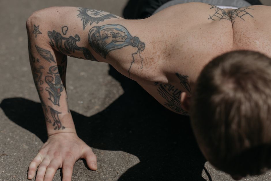 Shirtless man with tattoos performing push-ups on pavement, focusing on arm strength.
