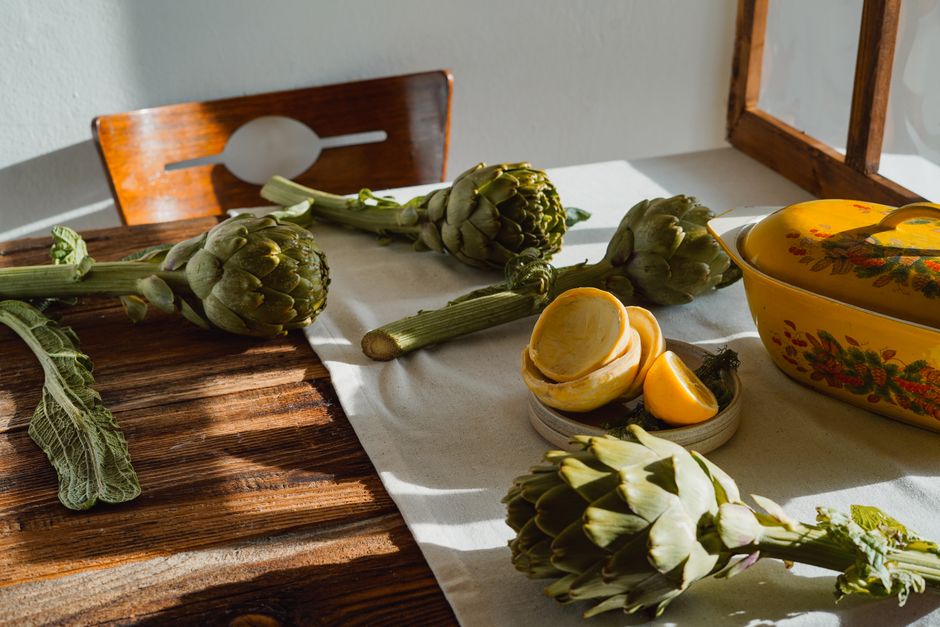 Sunlit rustic kitchen scene with fresh artichokes and sliced lemons on a wooden table.
