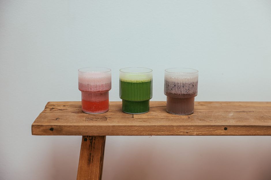 Three colorful beverages in glasses placed on a wooden bench, perfect for drinks themed content.