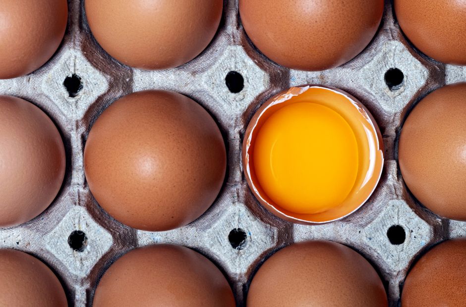 Top view of brown eggs in a carton with one cracked open, showcasing vibrant yolk.