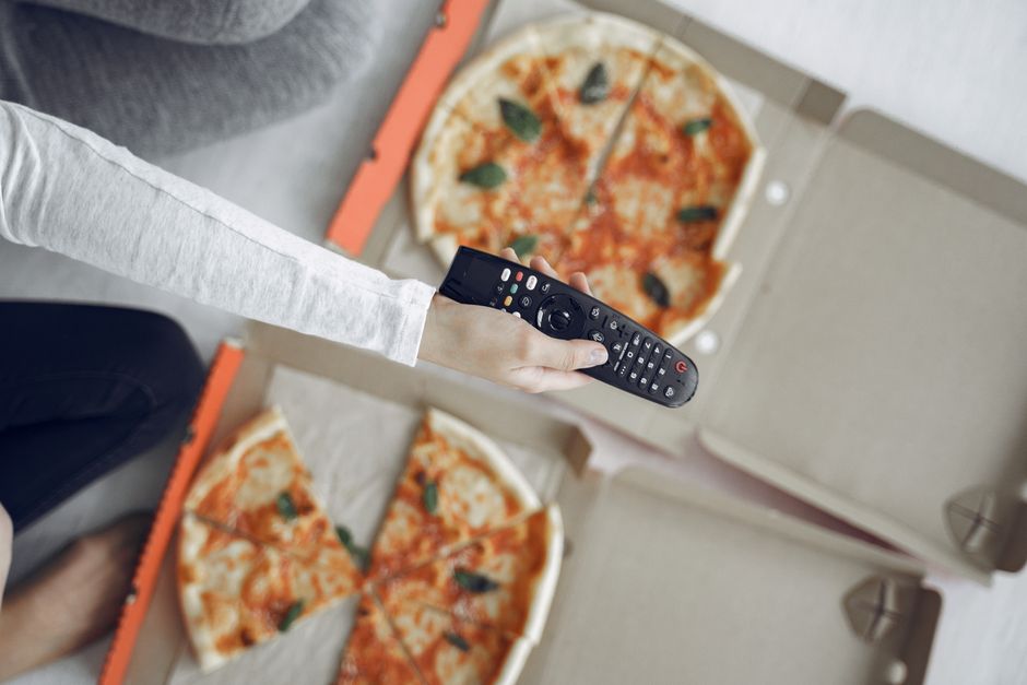 Top view of two pizzas and a remote control, perfect for a cozy movie night.