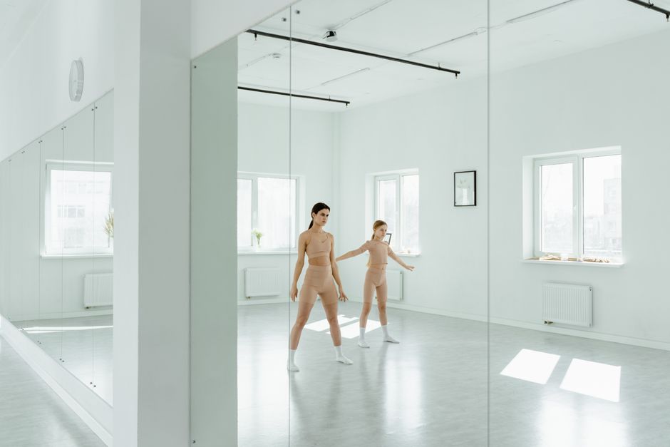 Two dancers practicing in a bright dance studio with mirrored walls.