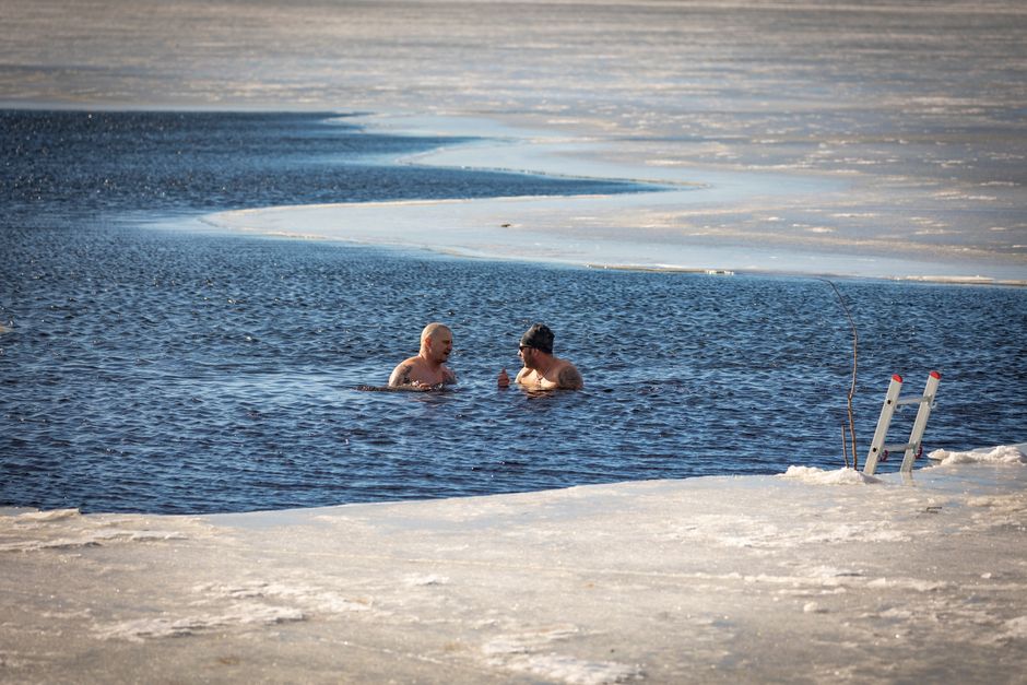 Two men brave the cold for a swim in a partially frozen lake during winter.
