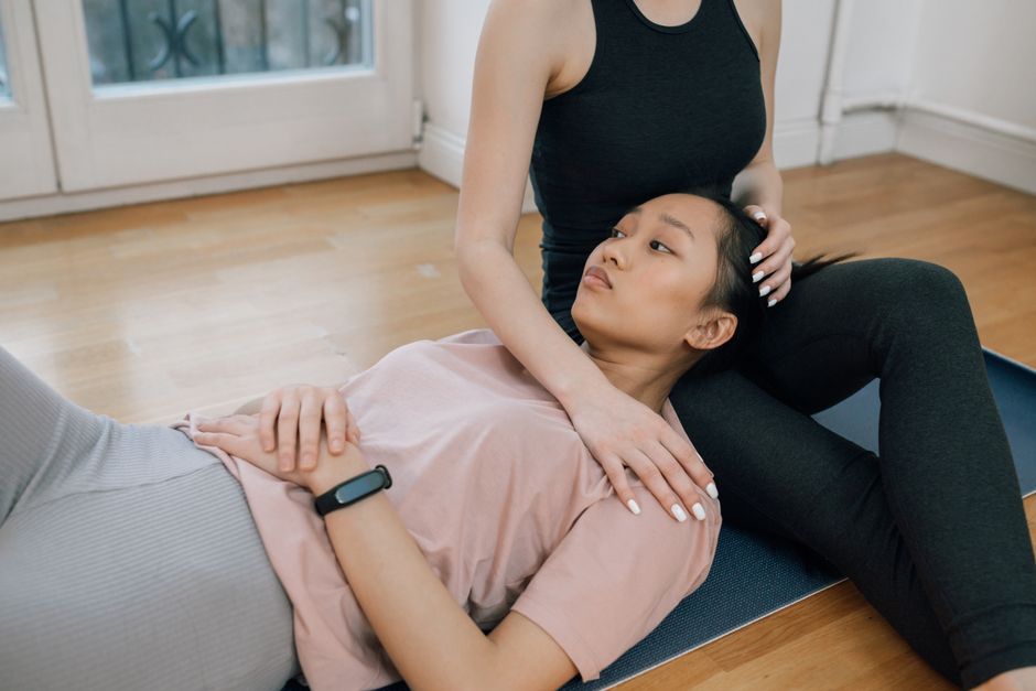 Two women engaging in a yoga session on a mat indoors, highlighting mindfulness and relaxation.
