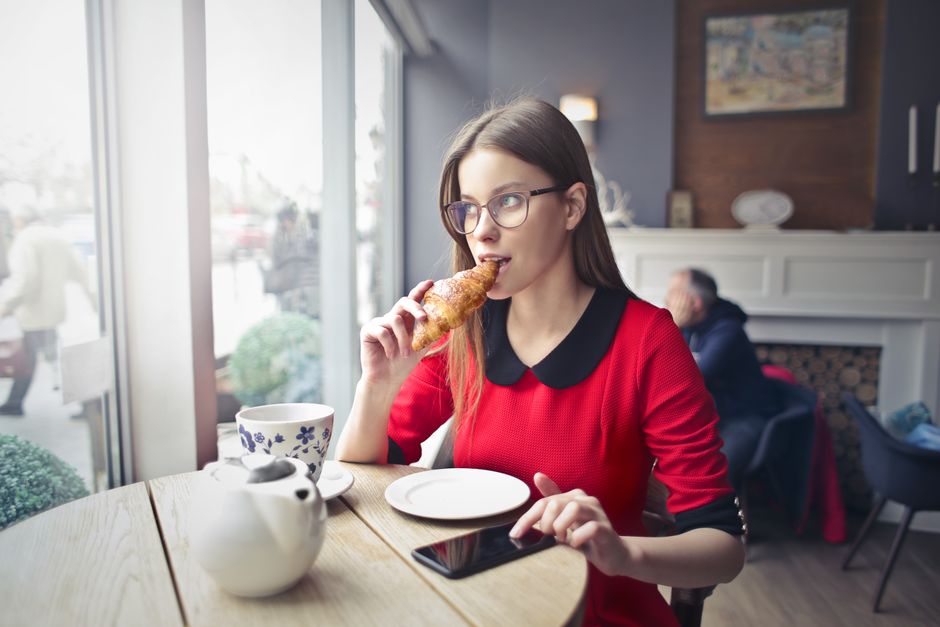 Woman enjoying a croissant with coffee at a cafe. Casual dining scene.