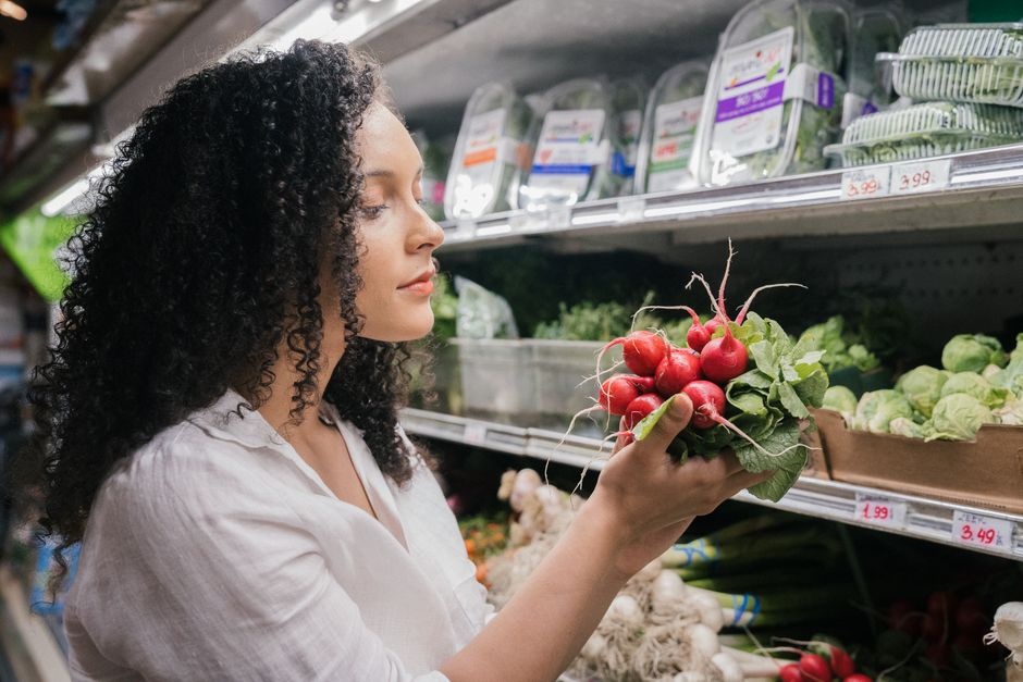 Woman in grocery store choosing fresh radishes from the vegetable aisle.