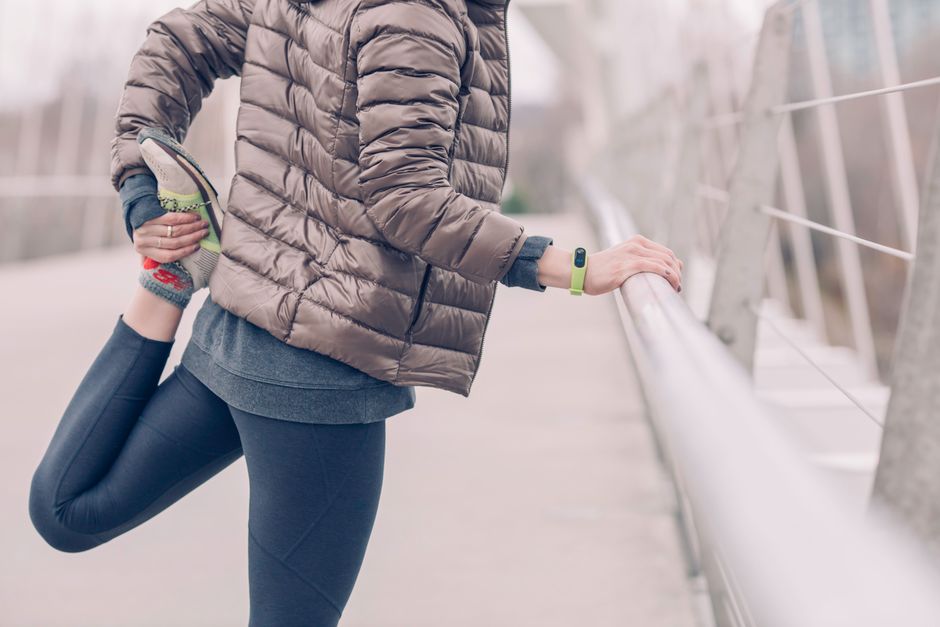 Woman in winter attire stretching outdoors on a bridge, fitness and lifestyle focus.