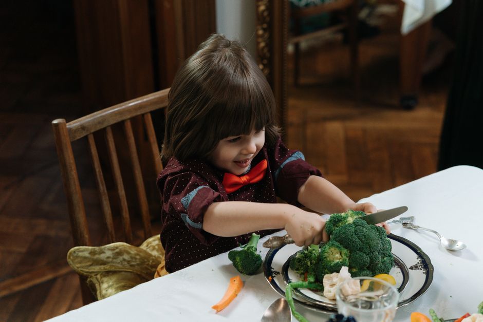 Young child excitedly cutting broccoli during a healthy meal at home.