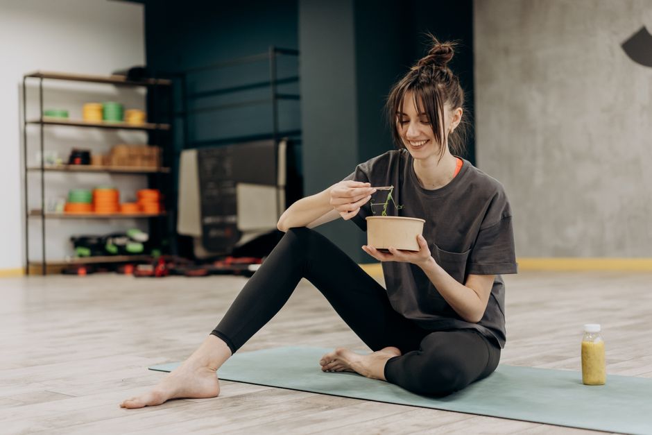 Young woman enjoying a healthy salad after exercising indoors. Promotes a balanced diet and fitness lifestyle.