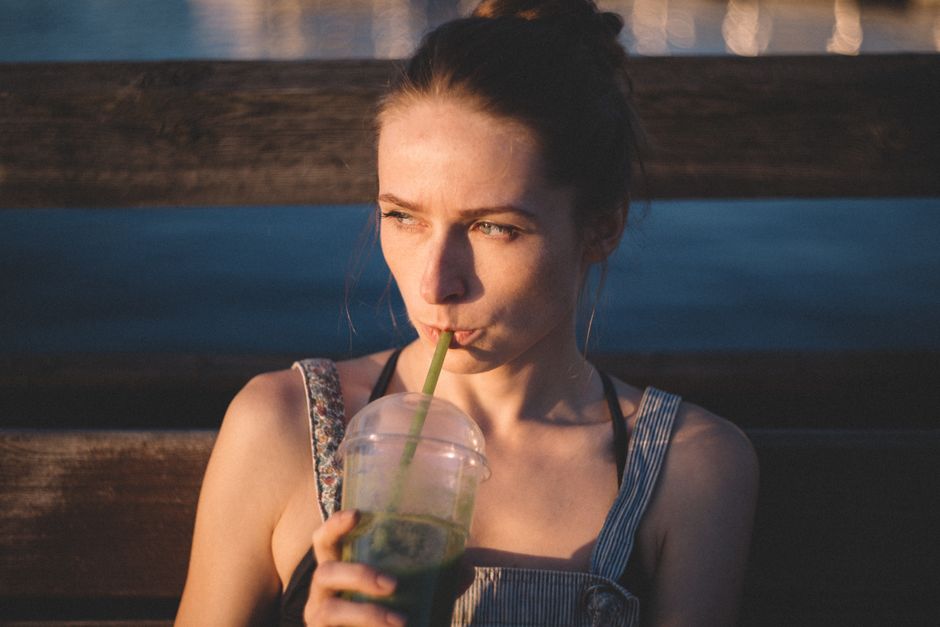 Young woman sipping a green smoothie outdoors on a sunny day, embodying lifestyle and relaxation.