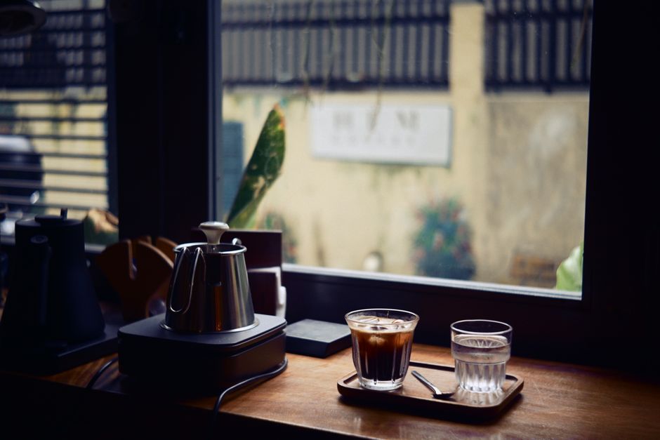 A cozy indoor cafe scene featuring a coffee and water on a wooden table by the window.