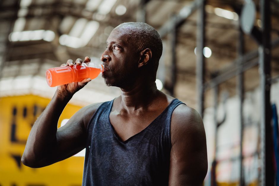A fit adult man drinks a cold beverage while taking a break from his workout at the gym.