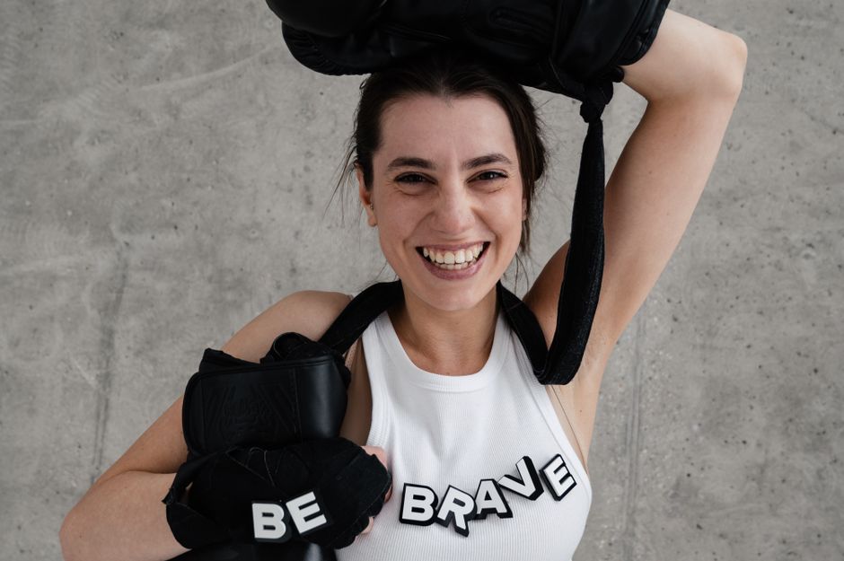 A joyful woman posing with boxing gloves and 'Be Brave' text, conveying empowerment.